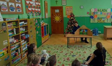 Nauczyciel prezentuje bajkę za pomocą teatrzyku kamishibai, dzieci siędzą przed nim.