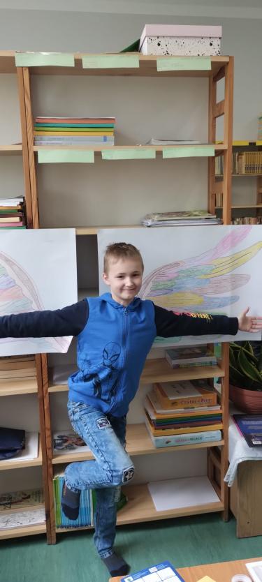 Uczeń pozuje na tle rysunku skrzydeł.