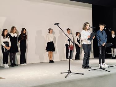 Występ uczniów SP nr 15 w Przemyślu - grupa dzieci stoi w tle, a dwoje recytuje wiersze do mikrofonu 