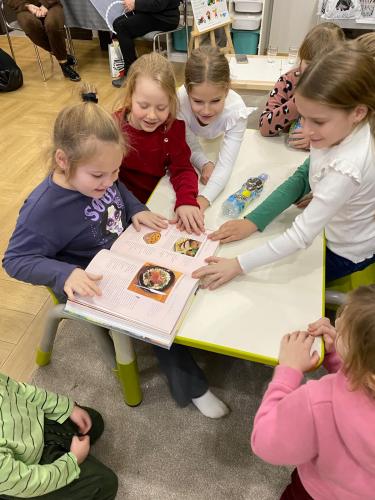 Dziewczynki  przeglądają przy stoliku książki związane z tradycjami bożonarodzeniowymi.